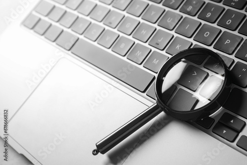 Magnifying glass and modern laptop on light grey table, closeup