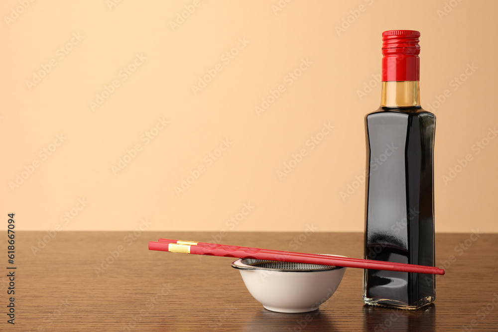 Bottle, bowl with soy sauce and chopsticks on wooden table against beige background. Space for text Bottle, bowl with soy sauce and chopsticks on wooden table against beige background. Space for text