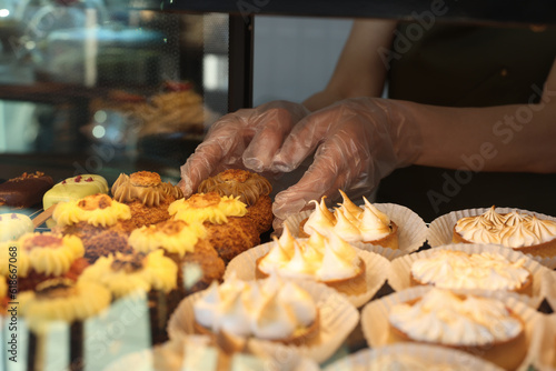 Seller taking delicious dessert from showcase in bakery shop, closeup