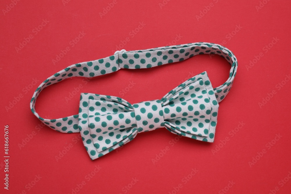 Stylish white bow tie with green polka dot pattern on red background, top view
