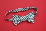 Stylish white bow tie with green polka dot pattern on red background, top view
