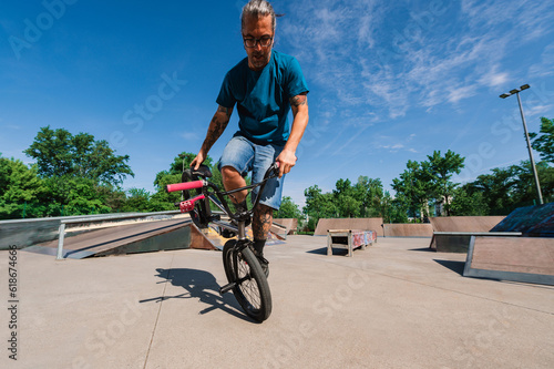 A professional middle-aged tattooed bmx rider is doing practice for the X-games in the skate park.