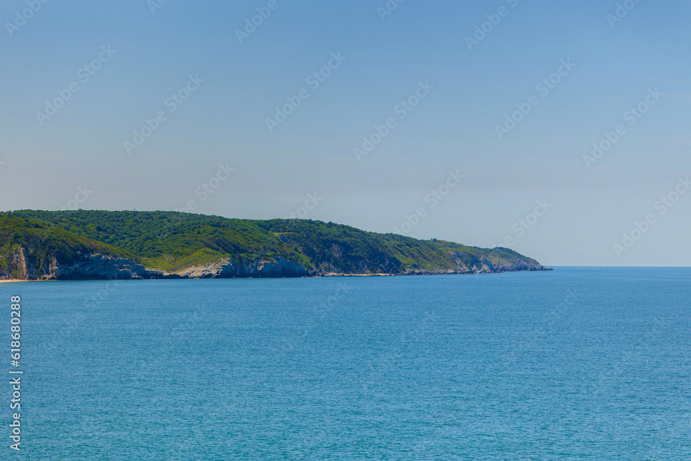 Promontory of sea shoreline with green forest on summer sunny day