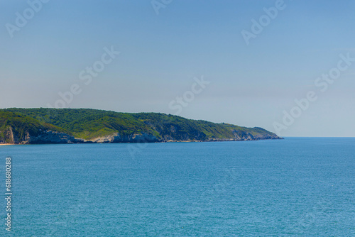 Promontory of sea shoreline with green forest on summer sunny day