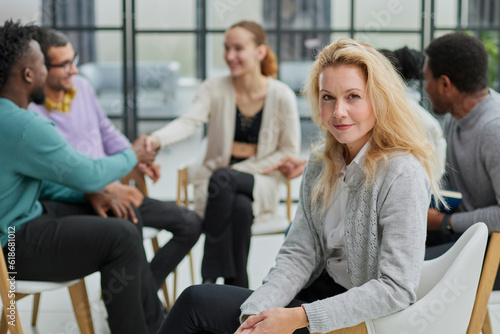 Smiling businesswoman looking at camera at seminar with her colleagues near by