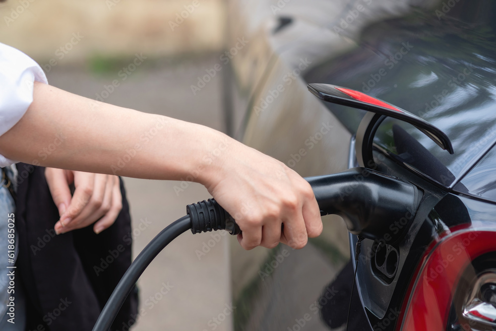 electric car or EV charging station A woman plugs in a black power cable to charge for clean energy for a trip eco concept and clean energy with electric vehicle technology. electric car or EV charging station A woman plugs in a black power cable to charge for clean energy for a trip eco concept and clean energy with electric vehicle technology.