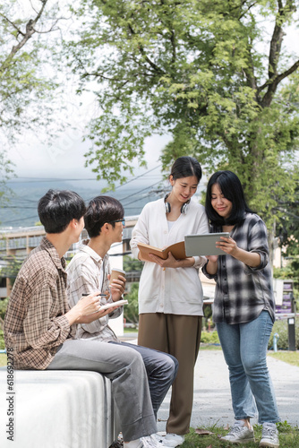 Group of Asian college student reading books and tutoring special class for exam on grass field at outdoors. Happiness and Education learning concept. Back to school concept. Teen and people theme.