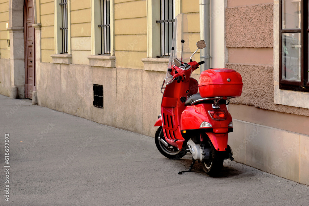 stylish red italian scooter. bright red vintage moped with storage box. old urban historic city setting. light gray cobblestone pavement. tourism, travel and vacationing concept. stucco exterior wall
