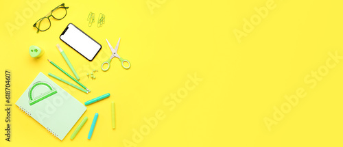 Mobile phone with eyeglasses and different stationery on yellow background. Banner for design