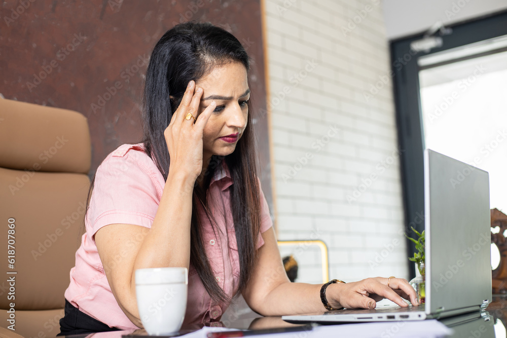 Tired and stressed mature indian businesswoman after working long hours in office. Workload headache and pain concept. Tired and stressed mature indian businesswoman after working long hours in office. Workload headache and pain concept.