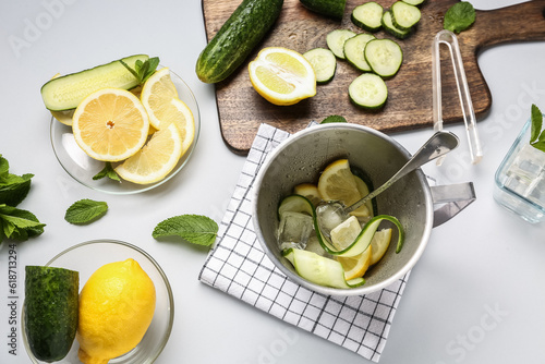 Bucket and bowls with ingredients for preparing cucumber lemonade on white background