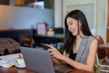 Close-up asian woman holding mobile phone in hand chatting with friends, plugged in headphones as listened music relieve stress while working in cafe bakery, expression relaxed when heard music.