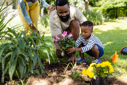 African american woman standing by father and son planting fresh flowers in field at yard