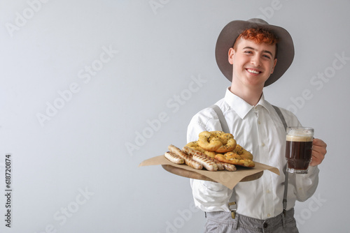 Young man in traditional German clothes with beer and snacks on light background