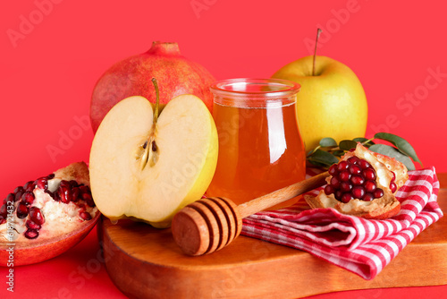 Bottle with jar of honey, pomegranate and apples for Rosh Hashanah celebration (Jewish New Year) on red background photo