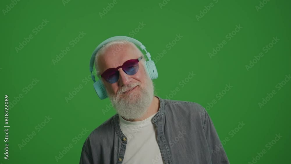Green Screen. Portrait of a Modern Old Man in the Funny Glasses Listens to Music in Headphones and Dancing. Emerging Technologies for Seniors. Green Screen. Portrait of a Modern Old Man in the Funny Glasses Listens to Music in Headphones and Dancing. Emerging Technologies for Seniors.