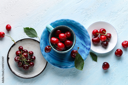 Cup and plates with sweet cherries on blue background