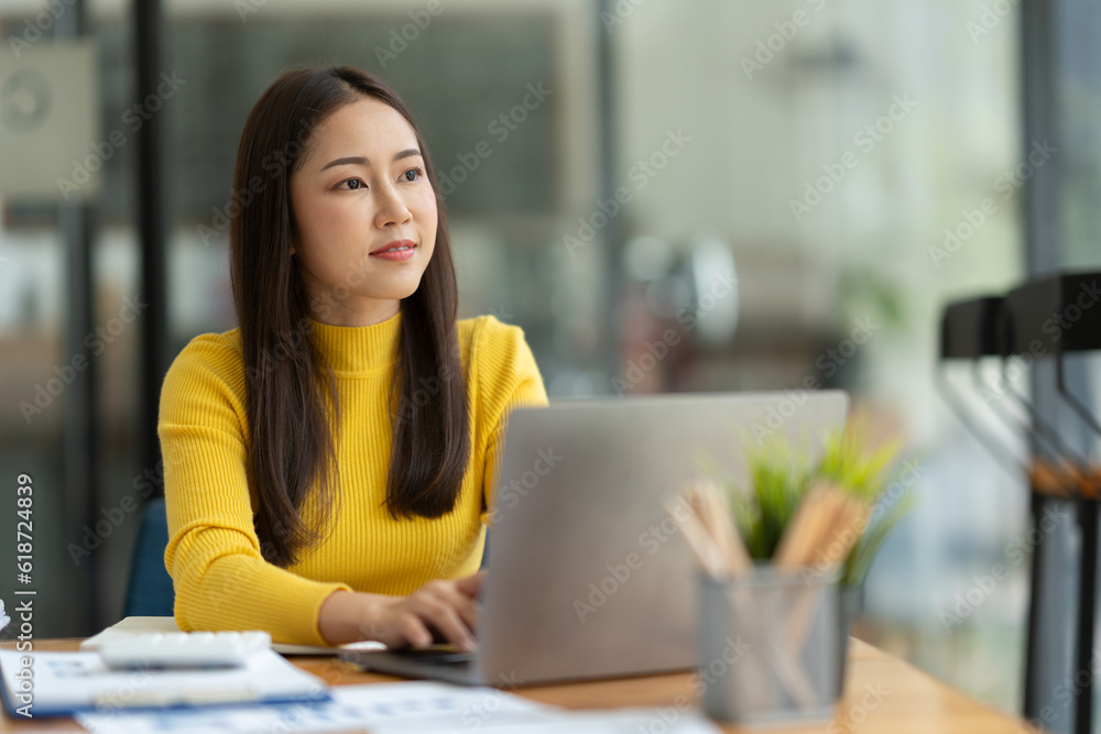 Confident Asian businesswoman using laptop computer working in office with calculator papers on table make a plan analyzing financial reports business plan investment analytical concept. Confident Asian businesswoman using laptop computer working in office with calculator papers on table make a plan analyzing financial reports business plan investment analytical concept.