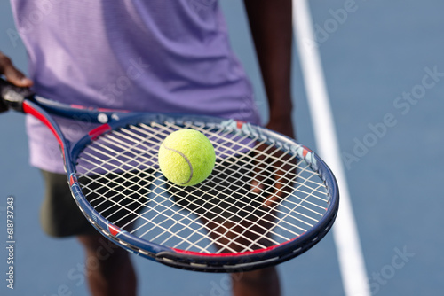 Midsection of african american male tennis player holding tennis racket and ball on outdoor court photo