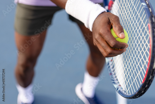 Midsection of african american male tennis player holding tennis racket and ball on outdoor court
