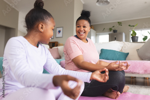 Happy african american mother and daughter doing yoga and meditating in living room photo