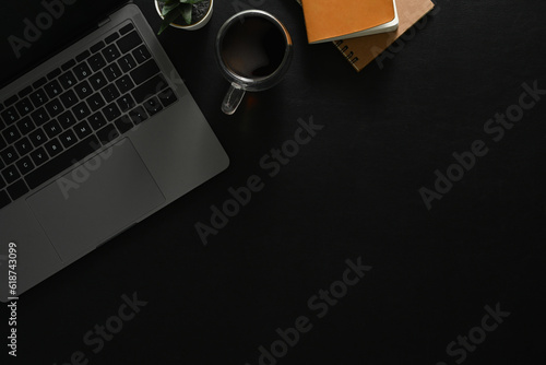Modern workplace, black office desk with laptop computer, cup of coffee and notebook. Top view with copy space