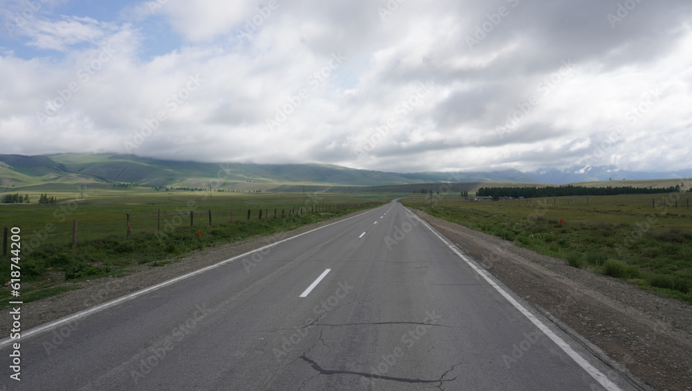 Fototapeta premium Road through the steppe to the mountains with clouds