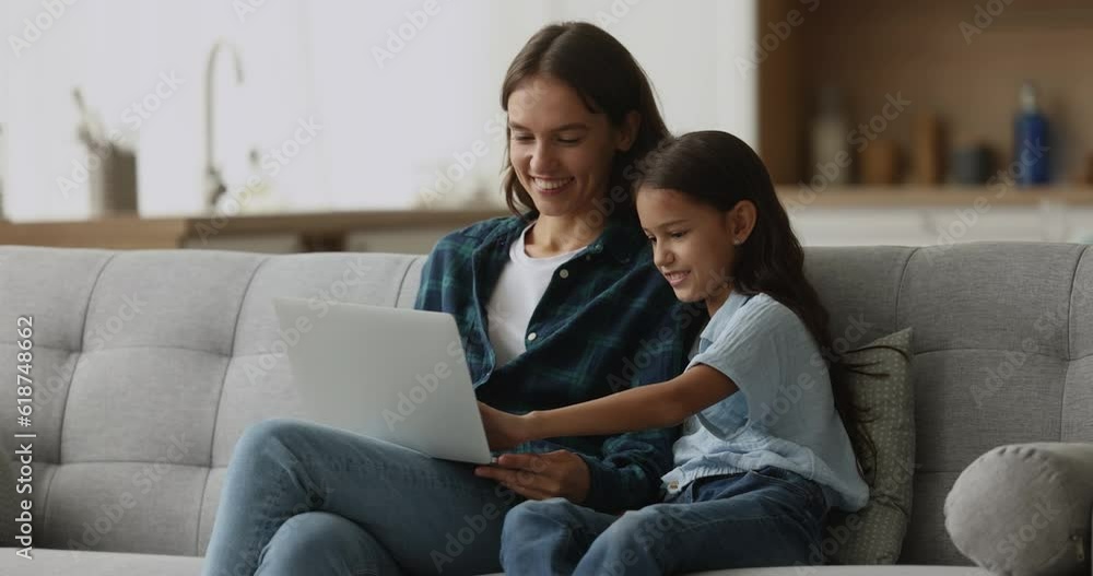 Happy young mother spend time with cute 10s daughter watch funny videos on-line on laptop, spend time on internet. Family leisure at home with modern wireless technology, electronic commerce clients Happy young mother spend time with cute 10s daughter watch funny videos on-line on laptop, spend time on internet. Family leisure at home with modern wireless technology, electronic commerce clients
