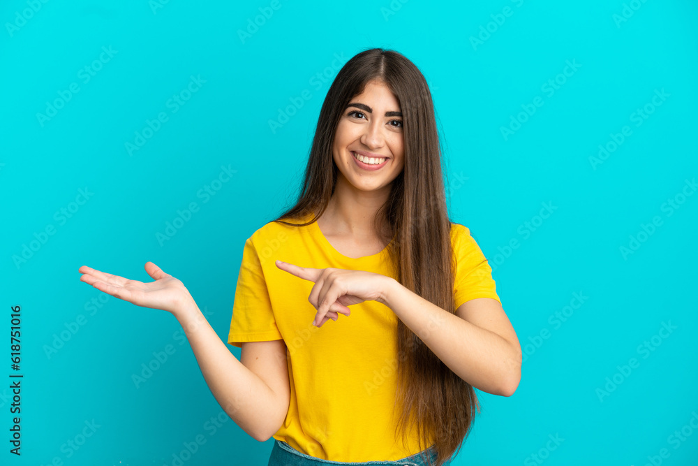 Young caucasian woman isolated on blue background holding copyspace imaginary on the palm to insert an ad Young caucasian woman isolated on blue background holding copyspace imaginary on the palm to insert an ad