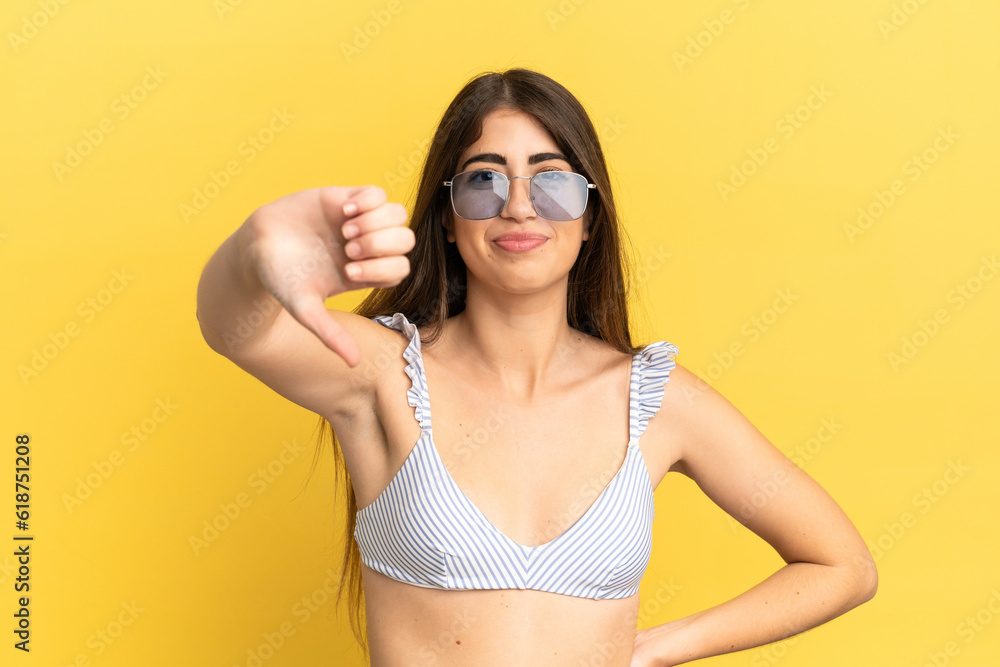Young caucasian woman in swimsuit in summer holidays isolated on yellow background showing thumb down with negative expression