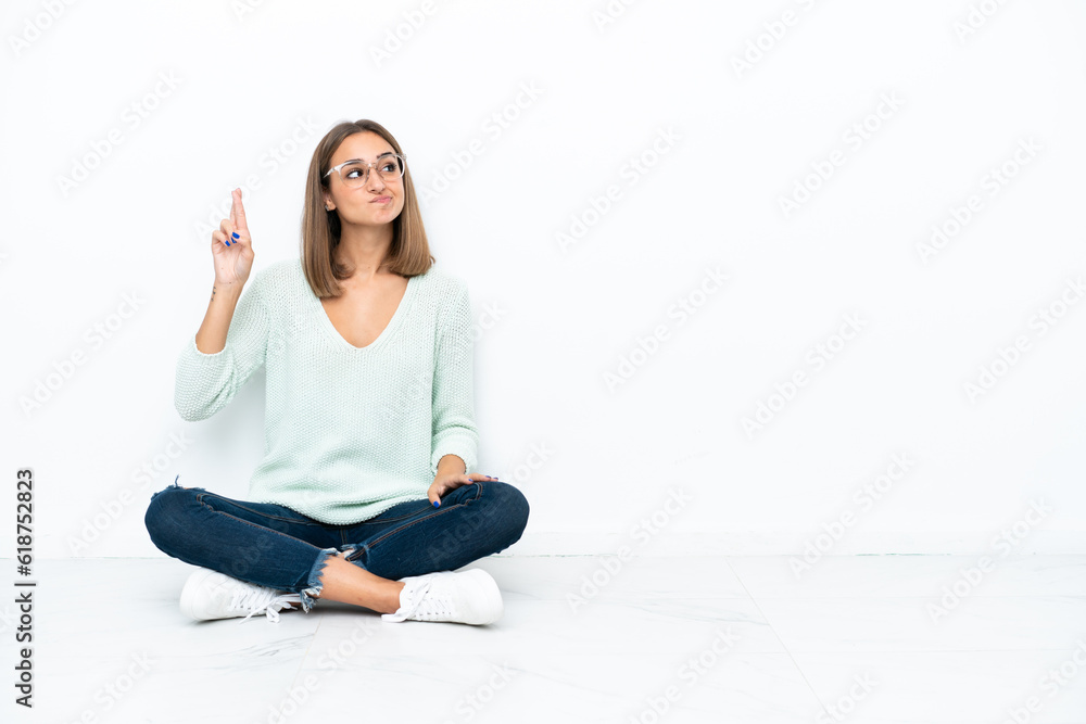 Young caucasian woman sitting on the floor isolated on white background with fingers crossing and wishing the best Young caucasian woman sitting on the floor isolated on white background with fingers crossing and wishing the best