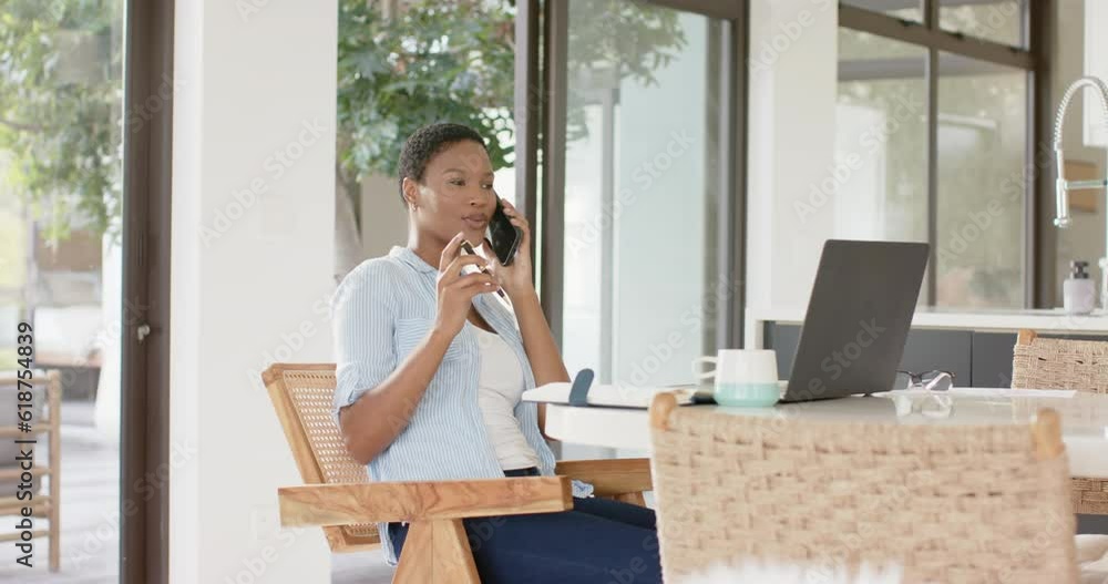 Happy african american woman sitting at table talking on smartphone and taking notes, slow motion Happy african american woman sitting at table talking on smartphone and taking notes, slow motion