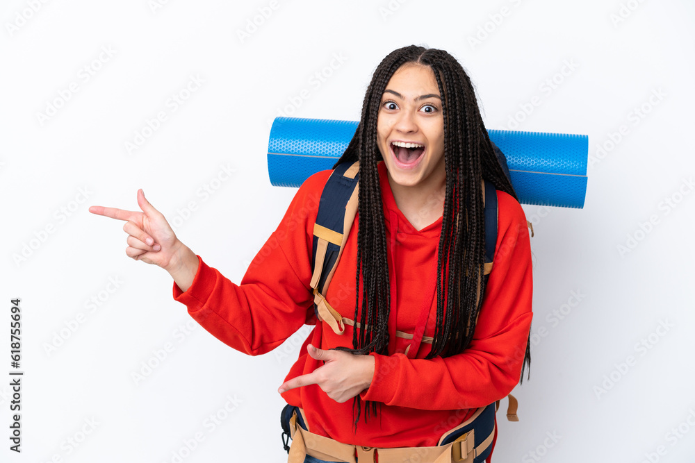 Hiker teenager girl with braids over isolated white background surprised and pointing side Hiker teenager girl with braids over isolated white background surprised and pointing side