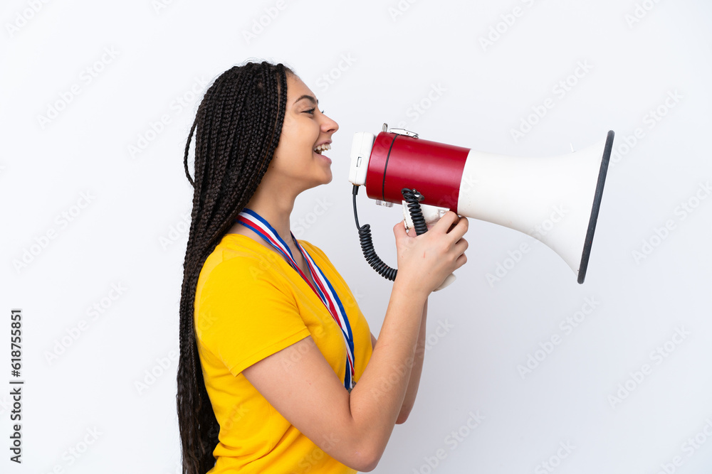 Naklejka premium Teenager girl with braids and medals over isolated pink background shouting through a megaphone