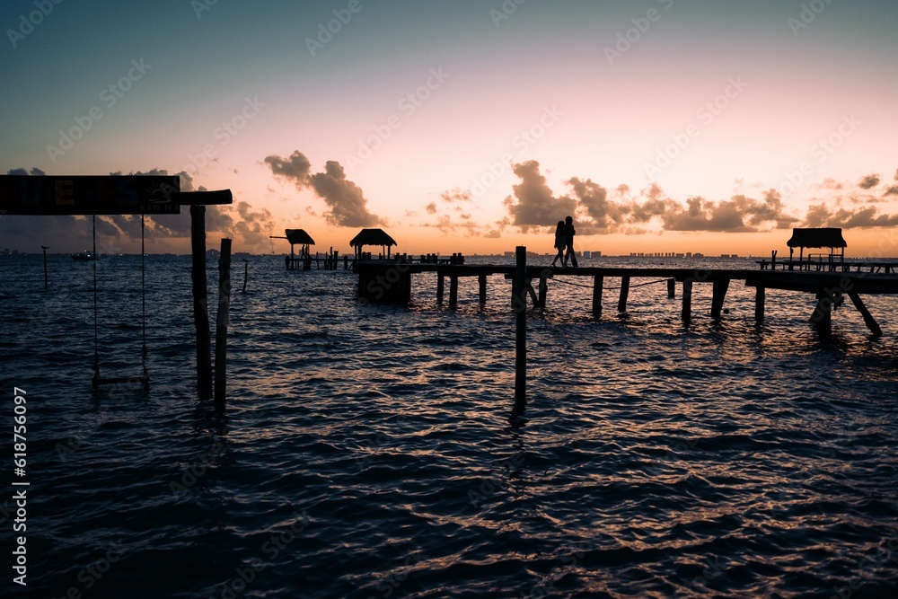 Tranquil scene of a lake shoreline at sunset, with a dock stretching out into the water