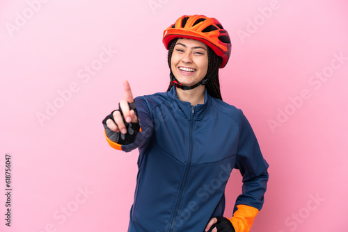 Teenager cyclist girl isolated on pink background showing and lifting a finger