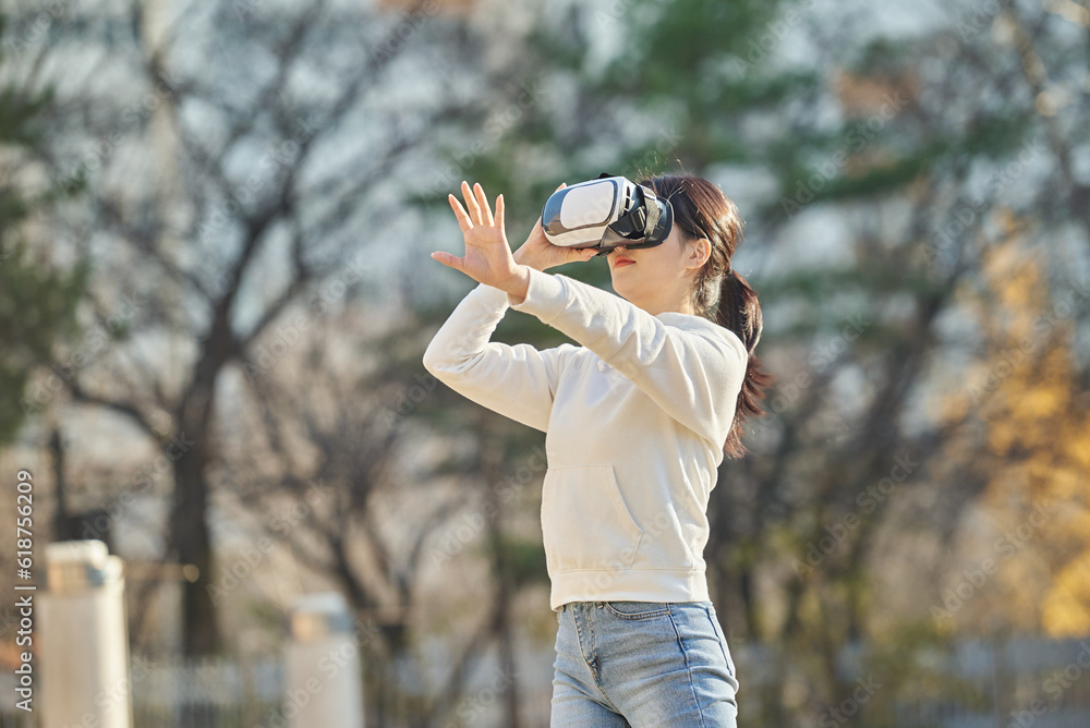 Young college student female model wearing 3D glasses and experiencing virtual reality in an outdoor autumn lawn plaza at a university in South Korea, Asia. Young college student female model wearing 3D glasses and experiencing virtual reality in an outdoor autumn lawn plaza at a university in South Korea, Asia.