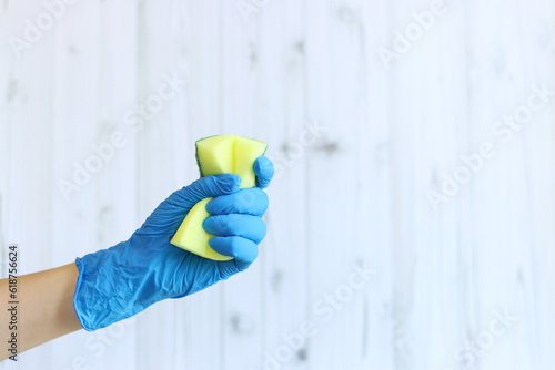 Sponge for washing dishes in a female hand on a light wood background. A hand in a latex glove holds a sponge for wet cleaning. Professional cleaning. Copy space