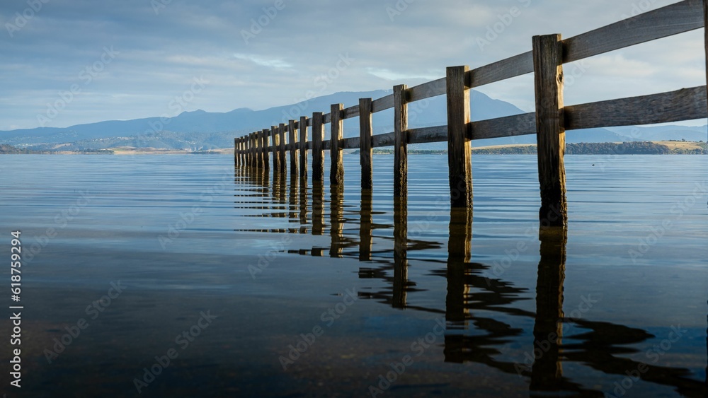 Narrow wooden pier extending to a tranquil lake, its reflection rippling in the sun.