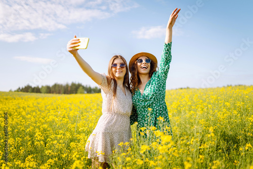 Selfie time.Two Young woman takes a selfie while walking flowering field. Nature, vacation, relax and lifestyle. Summer landscape.
