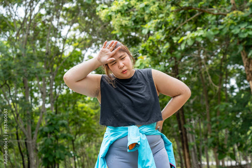 Overweight young woman with headache putting her right hand over her pain forehead during her morning exercise run at running track of a local park