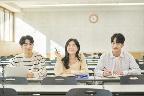 Three young Asian college students, both male and female, are in a classroom in South Korea where they are either teaching or studying