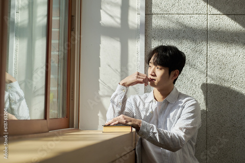 Picture of a young man who is a college student standing against a wall in a lecture hall at a university in South Korea. The room is bright
