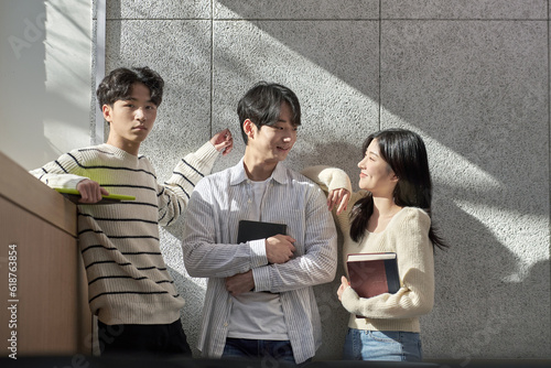 Model of a young male and female college student couple leaning against the wall of a university lecture hall in a light-filled room in South Korea, Asia. 