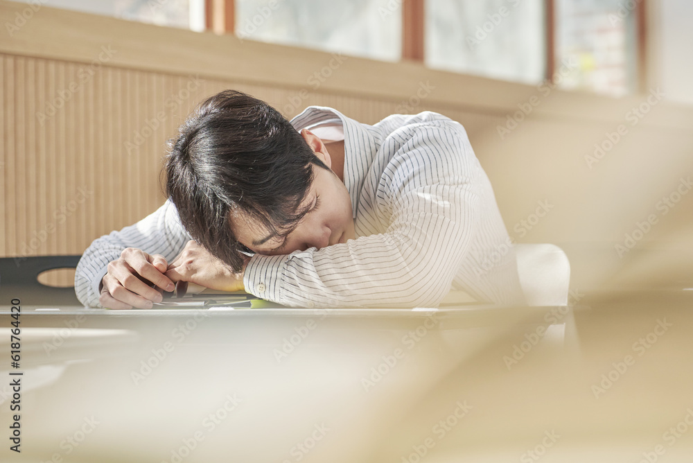 A young male college student is sleeping on his stomach on a desk inside a university classroom in South Korea, which is in Asia A young male college student is sleeping on his stomach on a desk inside a university classroom in South Korea, which is in Asia