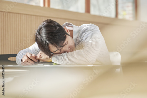 A young male college student is sleeping on his stomach on a desk inside a university classroom in South Korea, which is in Asia