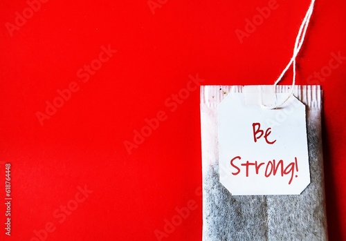Tea bag on red copy space background with text written BE STRONG, concept of self motivation and encouragement to build stronge mindset and get through hard times like teabag in hot water