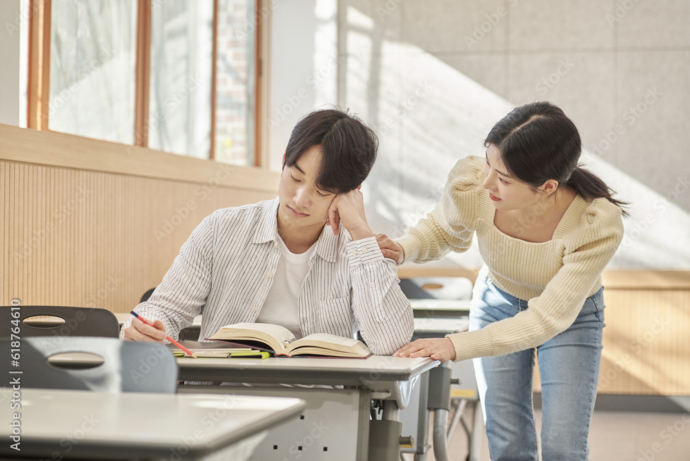 Obraz premium Girlfriend comforting a distressed young college male model sitting at a desk in a university classroom in South Korea, Asia