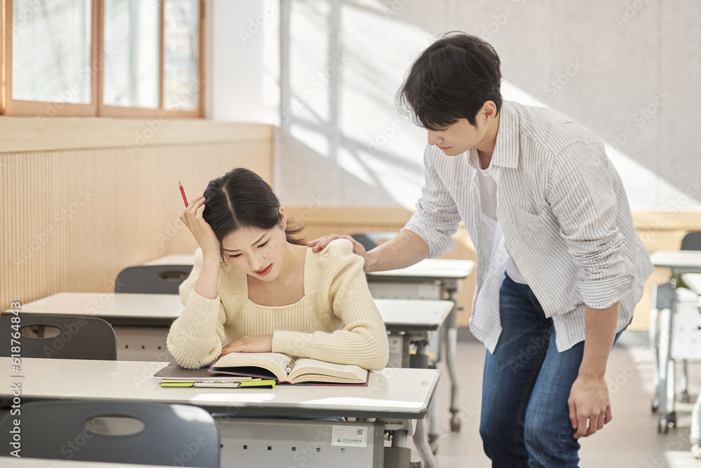 Obraz premium Colleague, friend, motivator, young male model comforting a distressed young female college student model sitting at a desk in a university classroom in Asia Korea. 