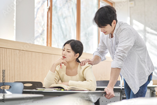 Colleague, friend, motivator, young male model comforting a distressed young female college student model sitting at a desk in a university classroom in Asia Korea. 